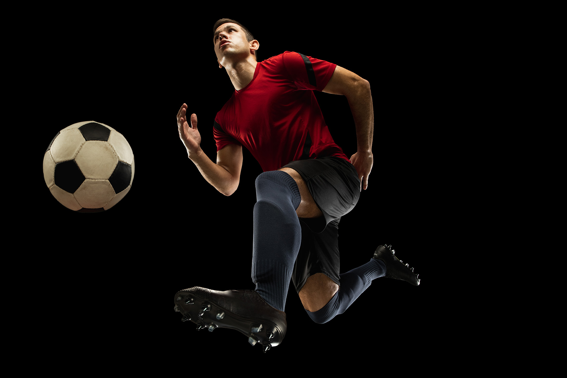 Young caucasian football, soccer player in action, motion isolated on black background, look from the bottom. Concept of sport, movement, energy and dynamic.